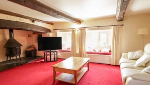 A cozy living room with a red carpet, a wooden table, a sofa, a TV, and a fireplace. - The Farmhouse (Keswick)