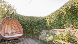 A wooden deck with a hanging wicker chair, surrounded by a stone wall and lush greenery. - The Farmhouse (Keswick)