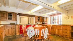 A kitchen with wooden cabinets, a red stove, and a dining area with wooden chairs and a table. - The Farmhouse (Keswick)