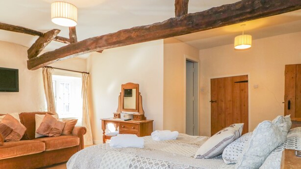 A bedroom with a large bed, a wooden dresser, a mirror, a wooden door, and a brown sofa. - The Farmhouse (Keswick)