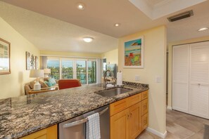 A kitchen with granite countertops, wooden cabinets, a stainless steel sink, and a view of the outdoors through large sliding glass doors. - 4th Floor Condo with Water Views (Treasure Island)