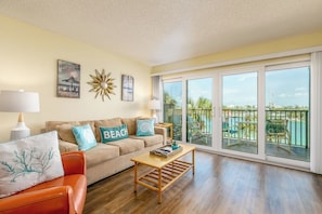A spacious living room with a beige sofa, a wooden coffee table, and a view of a pool and ocean through large sliding glass doors. - 4th Floor Condo with Water Views (Treasure Island)