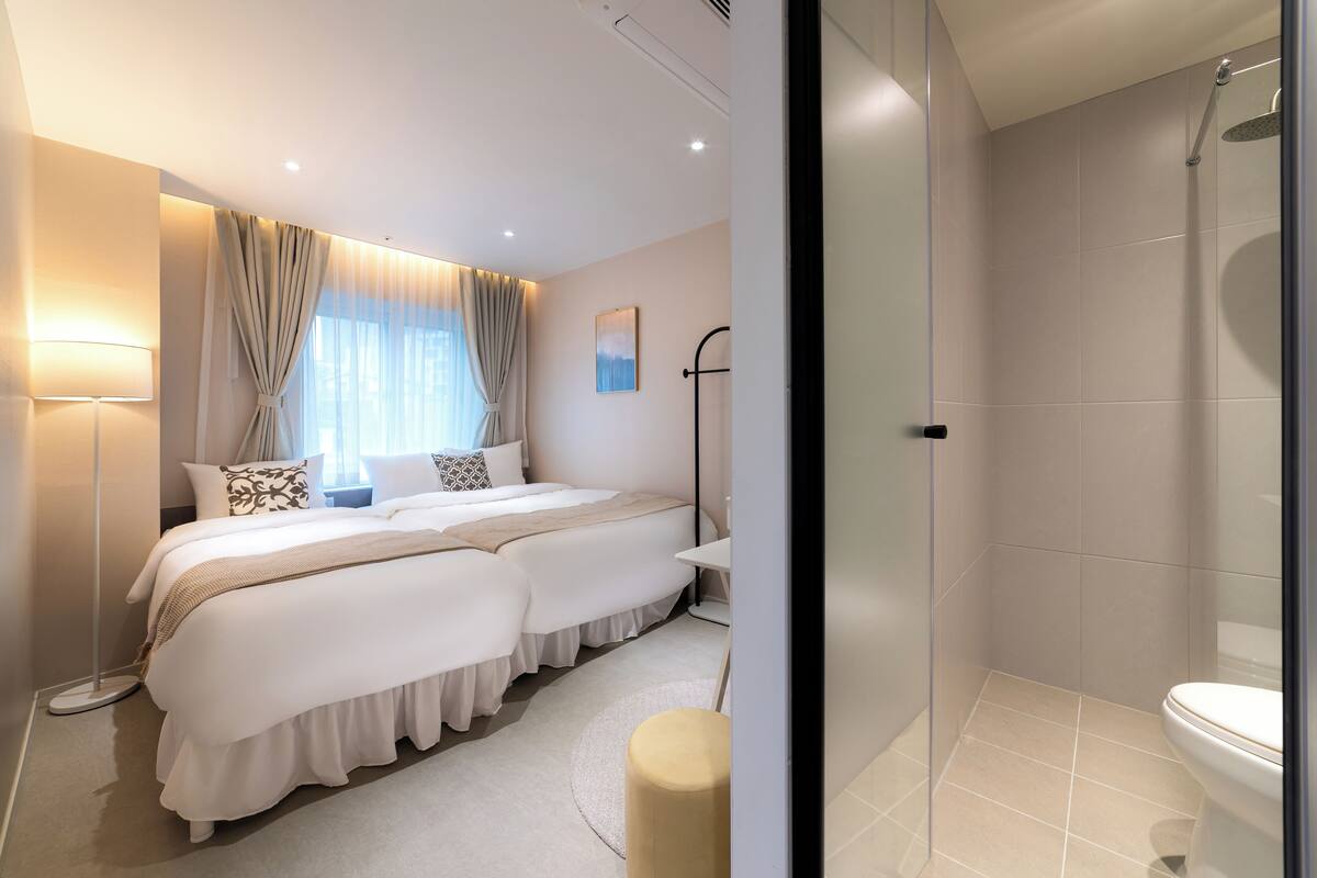 Habitación de hotel moderna con una cama grande, mesitas de noche, una lámpara de pie y una zona de ducha.