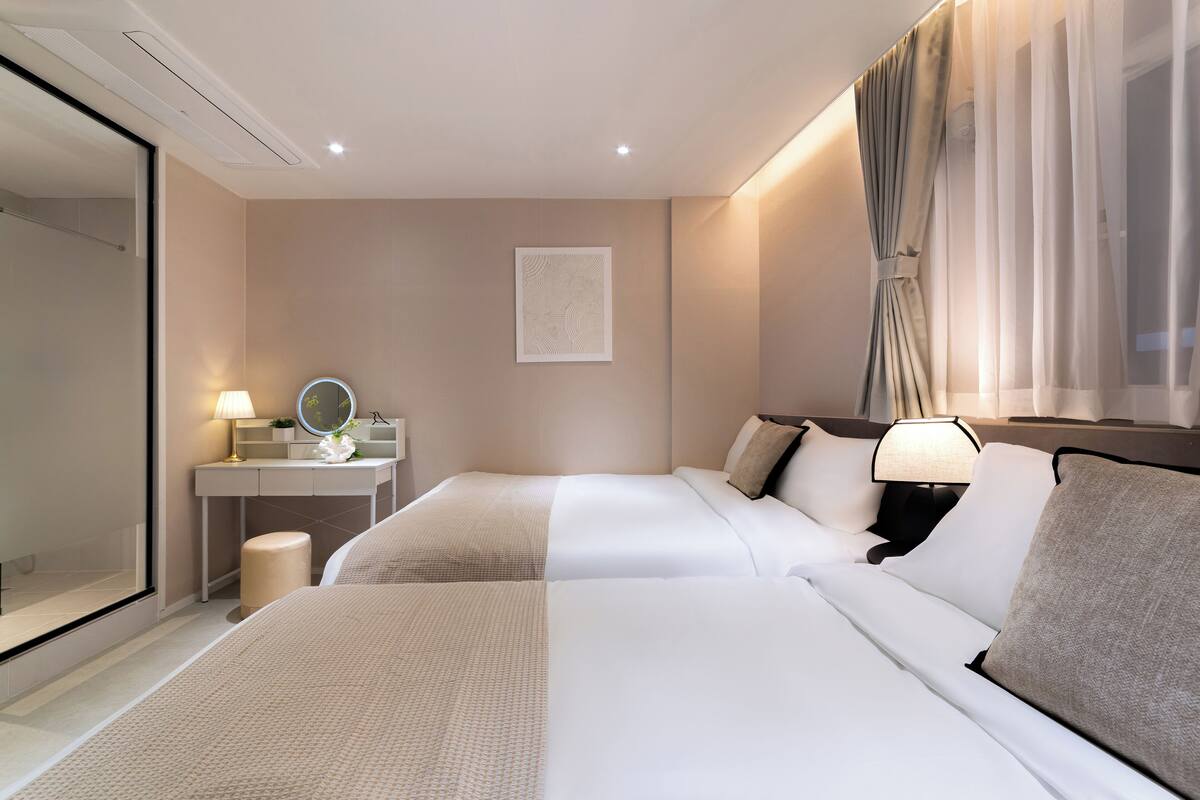 Habitación de hotel con dos camas, una mesita de noche con lámpara, un espejo y una obra de arte en la pared.