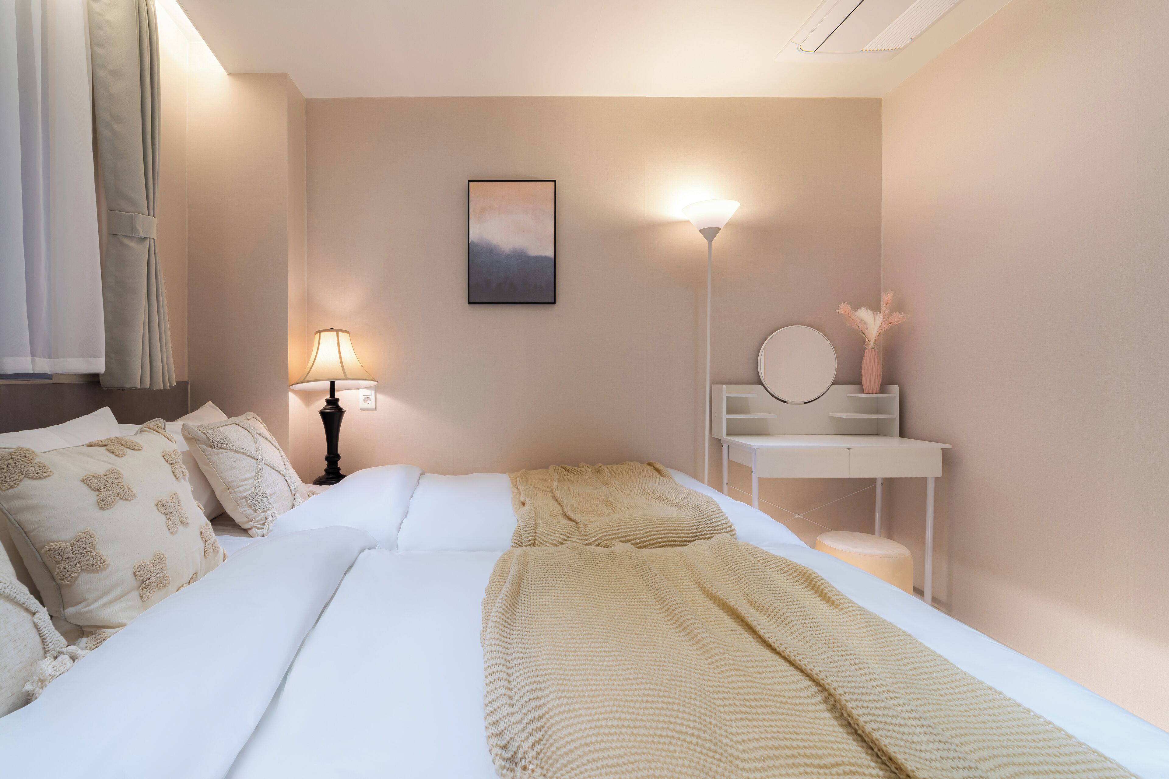 Een keurig opgemaakt slaapkamer met een bed, nachtkastje, lamp en een spiegel aan de muur.