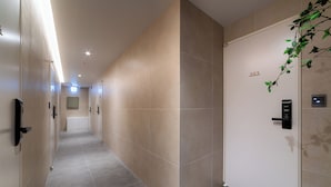 Ein Korridor mit beige gestrichenen Wänden und grauen Fliesen, eine Tür mit der Nummer 303 sowie ein an der Wand befestigtes Gegensprechanlage.