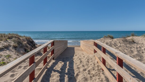 Een houten looppad dat naar het strand leidt, met helderblauwe lucht.