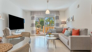 Een moderne woonkamer met een flatscreen televisie, een bank, een eettafel en uitzicht op de buitenruimte door een glazen deur.