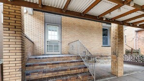 Ein Backsteinhaus mit einer Holzdachterrasse und einer Metalltreppe, die zu einer Tür führt.