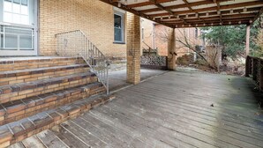 Eine Holzterrasse mit einer Ziegelstufenanlage, die zu einer überdachten Veranda führt.