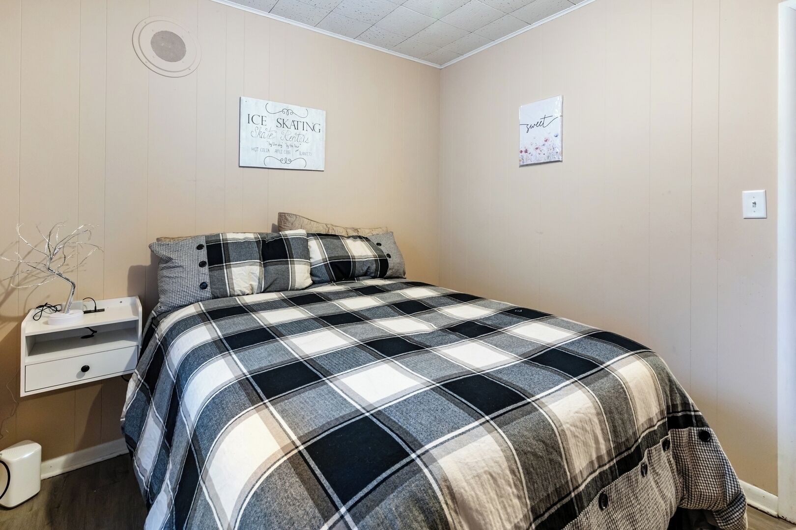 Une chambre à coucher avec une couvre-lit à carreaux, une table de chevet avec une lampe et deux éléments décoratifs sur les murs.