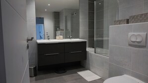 A modern bathroom with a glass shower enclosure, a white sink, and a dark-toned vanity.