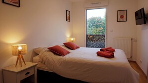 A bedroom with a bed, two bedside lamps, a window with a view of trees, and a radiator.