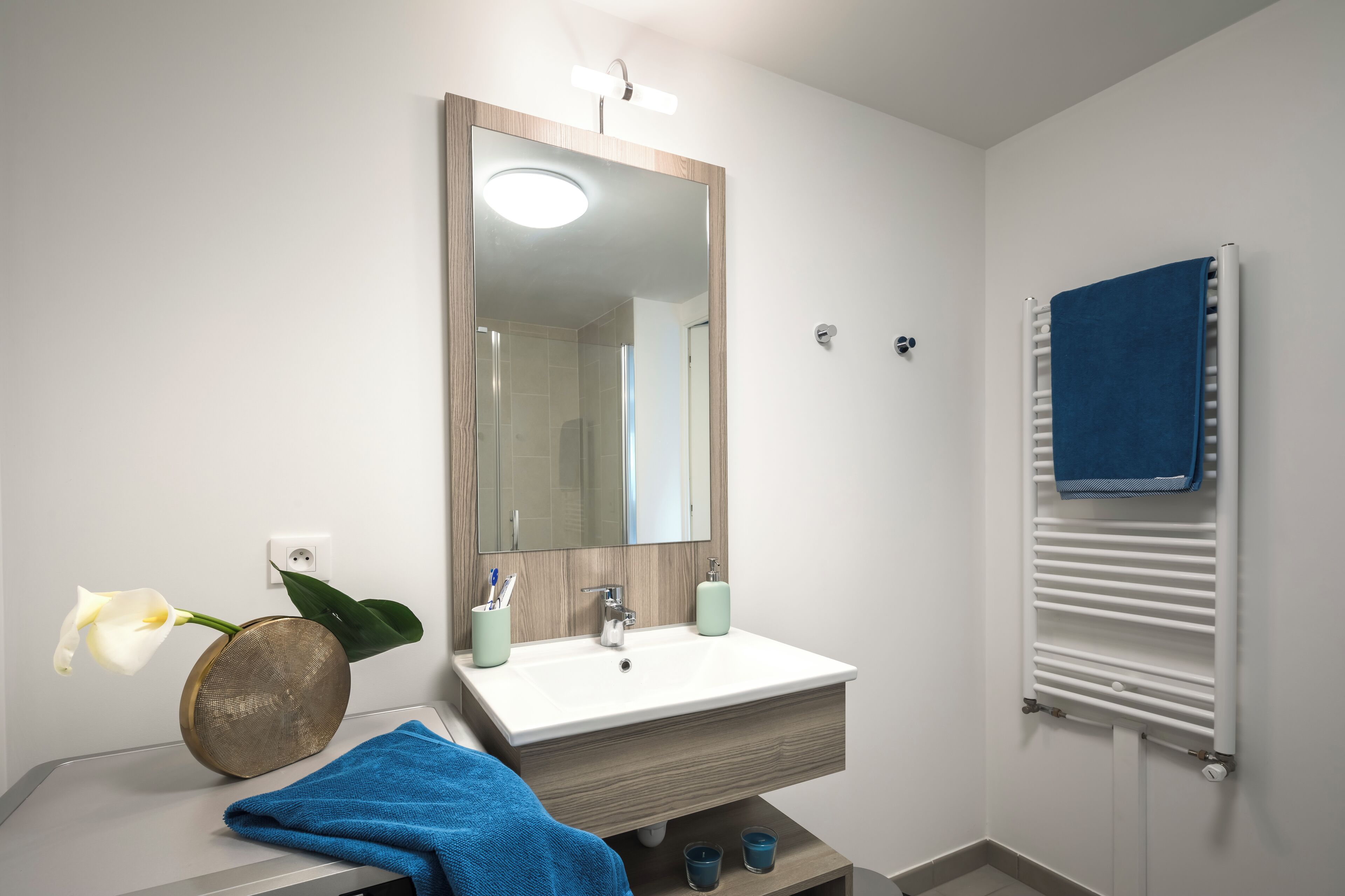 Un baño con lavamanos blanco, espejo, toallero y un florero.