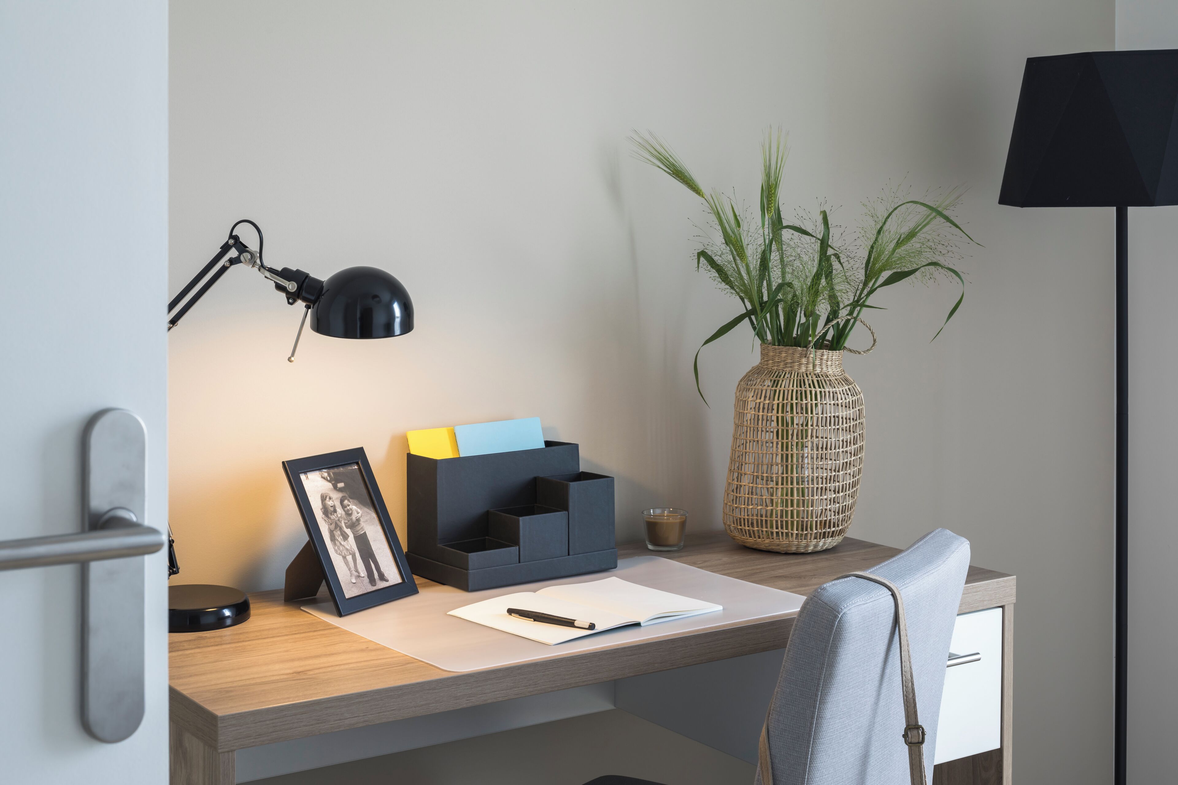 A desk with a lamp, a picture frame, a vase with plants, and a notebook.