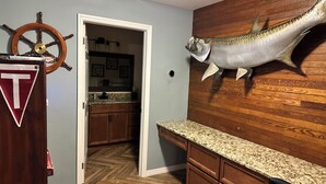 Ein Zimmer mit einer Holzwand, einem aufgehängten Fisch, einem Holzschrank und einer Tür, die in eine Küche führt.