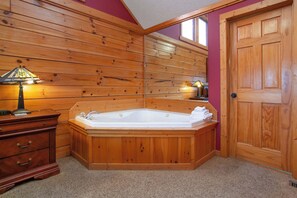 A wooden cabin interior with a hot tub, wooden walls, a door, and a dresser with a lamp. - Spectacular 4BR Cabin w/ Game Room, Hot Tub, Views (Gatlinburg)