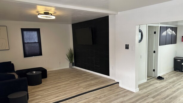A modern living room with a wooden floor, a black sofa, a small round table, and a potted plant. - Beautiful 2-bedroom house in tranquil Warren perfect for relaxing stays (Warren)