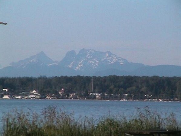 A coastal view with a mountain range in the background, a body of water in the foreground, and a small settlement with buildings along the shore.