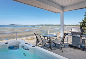 A covered outdoor area with a hot tub, a grill, and a table with chairs.