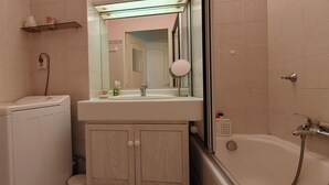 Une salle de bain équipée d’un lave-linge, d’un lavabo avec un miroir et d’une baignoire.