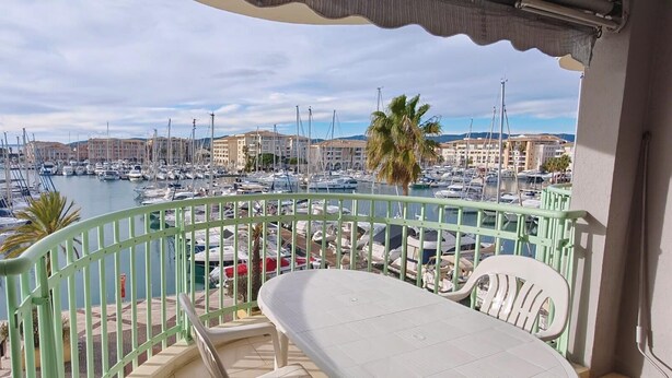 Un balcon donnant sur une marina remplie de bateaux, avec un palmier et des bâtiments en arrière-plan.
