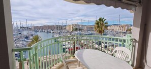 Uma varanda com vista para uma marina repleta de barcos, uma palmeira e edifícios ao fundo.