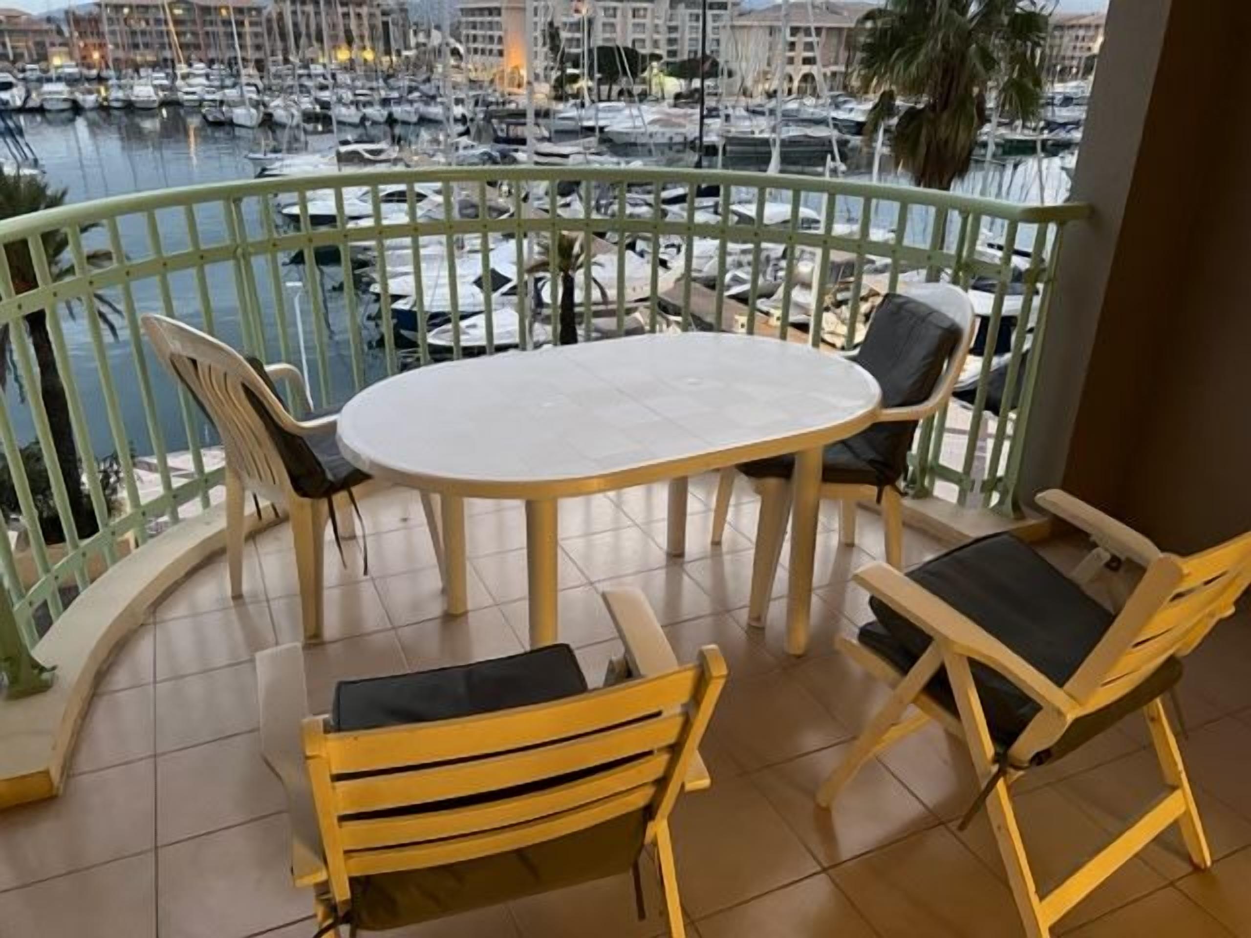 A balcony with a round table and four chairs, overlooking a marina with boats.