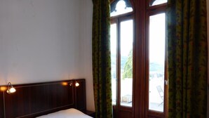 Ein Hotelzimmer mit einem Bett, einem Nachttisch, einem Fenster mit Vorhängen und Blick ins Freie.
