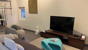 Moderni olohuone, jossa on suuri litteänäyttöinen televisio, sohva, meditaatioon tarkoitettu erillinen tila ja pieni patsas.