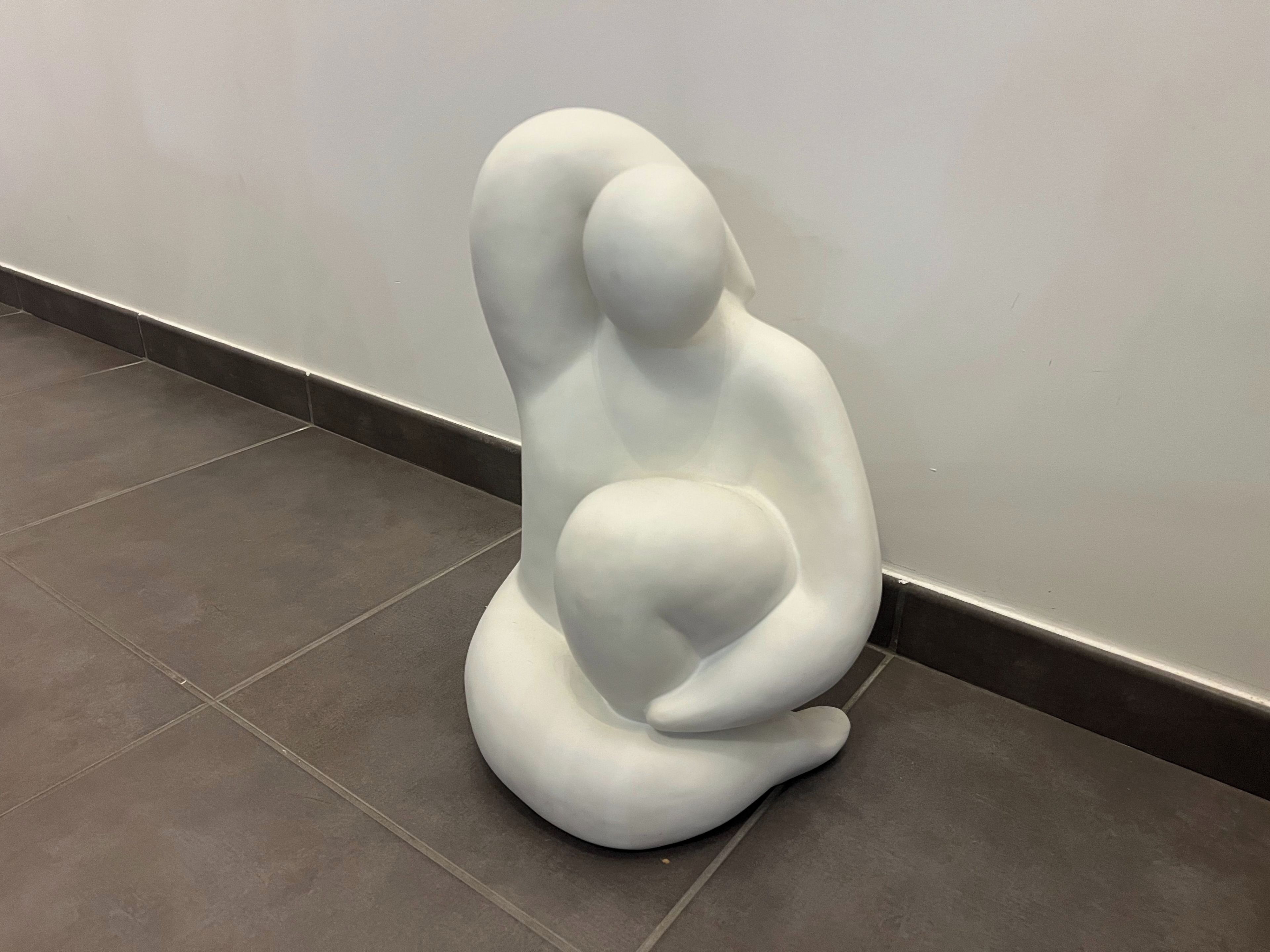 Eine weiße, abstrakte Skulptur auf einem gefliesten Boden vor einer schlichten Wand.
