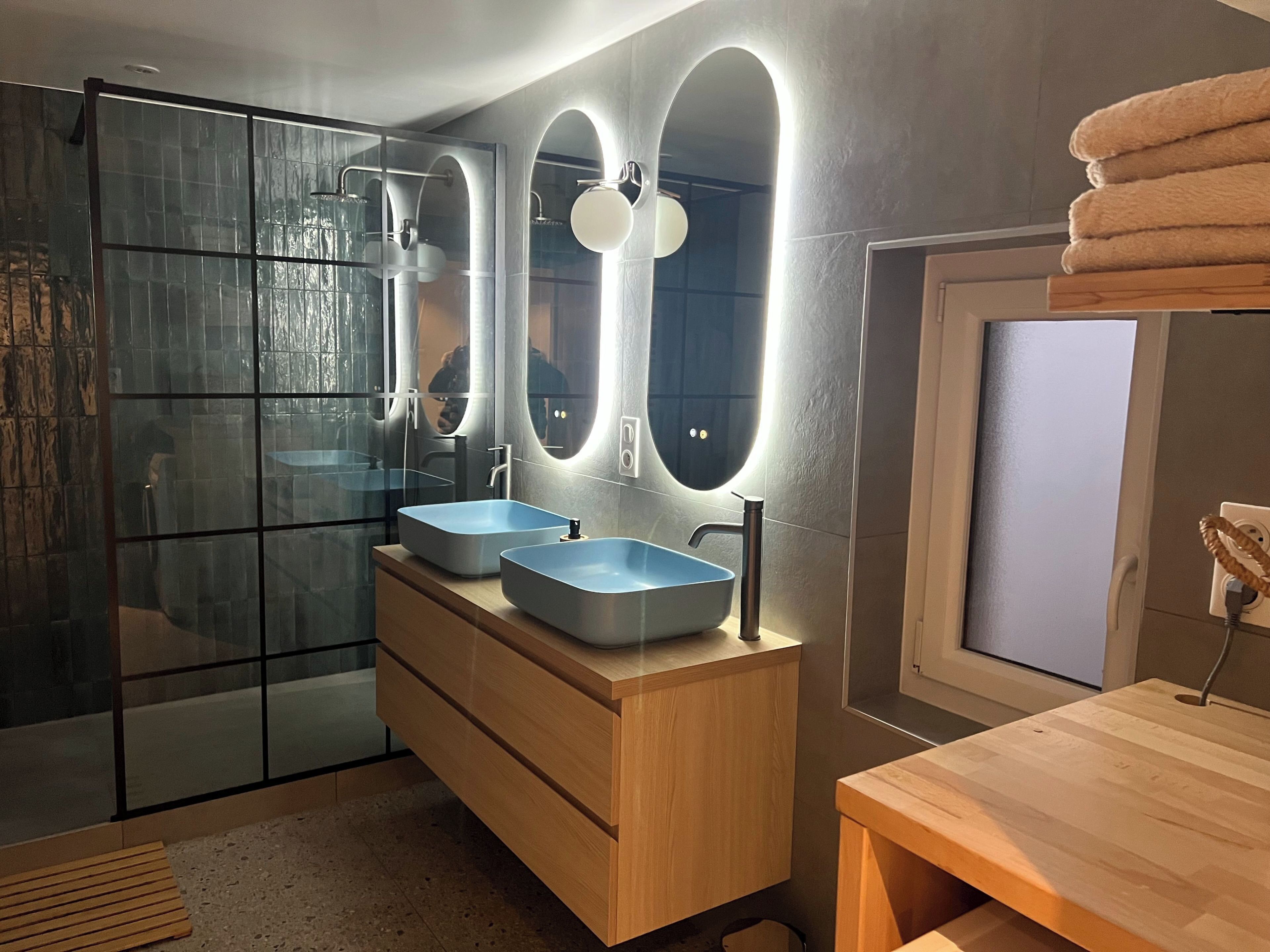 Un baño moderno con dos lavamanos, cabina de ducha con mampara de vidrio y tocador de madera.