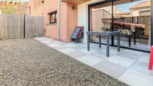 A patio area with a table and chairs, a wooden fence, and a gravel path. - Modern townhouse with parking (Toulouse)