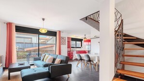 A modern living room with a sofa, dining table, and chairs, a staircase, and a kitchen in the background. - Modern townhouse with parking (Toulouse)
