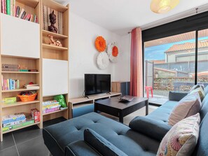 Een moderne woonkamer met een bank, televisie, boekenkast en uitzicht op het buiten.