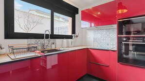 A modern kitchen with red cabinets, a Bosch oven, and a window with a view of a building and bare trees. - Modern townhouse with parking (Toulouse)