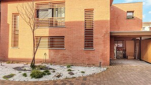 A modern two-story brick house with large windows and a small garden area with white gravel and greenery. - Modern townhouse with parking (Toulouse)