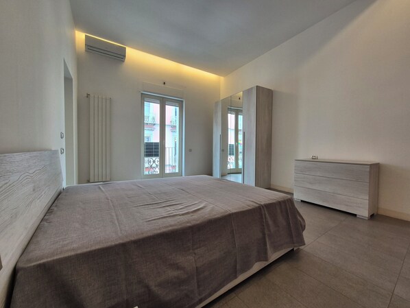 Ein Schlafzimmer mit Bett, Kommode und einer Schiebetür, die auf einen Balkon führt.