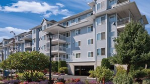 A multi-story residential building with balconies, a parking garage, and landscaped gardens. - Birch Bay | Group Beach Retreat | Pool + Beach | 2BR (Blaine)