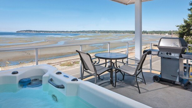 A covered outdoor area with a hot tub, a grill, and a table with chairs. - Birch Bay | Group Beach Retreat | Pool + Beach | 2BR (Blaine)