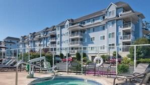 A swimming pool with lounge chairs, a poolside area, and a multi-story building with balconies in the background. - Birch Bay | Group Beach Retreat | Pool + Beach | 2BR (Blaine)