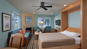 A hotel room with a bed, a seating area with chairs, a fireplace, a television, and a ceiling fan. - Birch Bay | Group Beach Retreat | Pool + Beach | 2BR (Blaine)