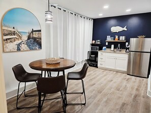 Une cuisine moderne avec des meubles blancs, un réfrigérateur en acier inoxydable et un coin repas comprenant une table ronde et deux chaises.