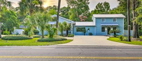 A two-story house with a blue exterior, surrounded by well-maintained landscaping and palm trees.