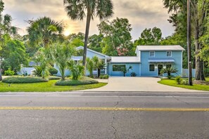 Een tweelaags huis met een blauwe gevel, omringd door verzorgde beplanting en palmbomen.