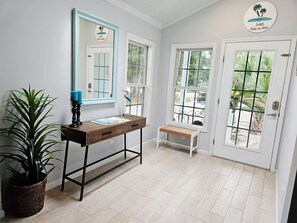 Une pièce avec un bureau en bois, un banc, un grand miroir et une porte donnant sur une vue agréable.