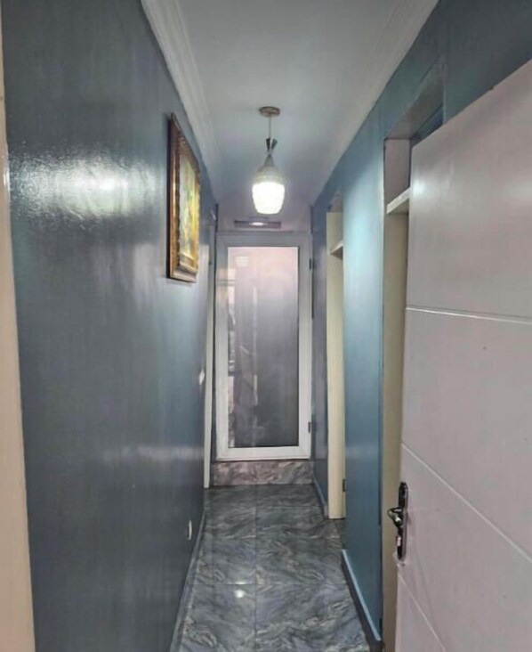A narrow hallway with a marble floor, a ceiling light, and a door at the end.