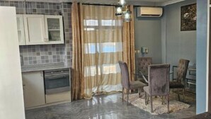 A modern kitchen with white cabinets, a built-in oven, and a dining area with a table and chairs. - Great stay (Kinshasa)