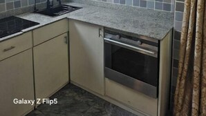 A compact kitchen with white cabinets, a built-in dishwasher, and a window. - Great stay (Kinshasa)