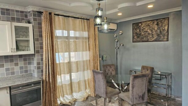 A modern kitchen with a dining area, featuring a glass table, chairs, and a pendant light. - Great stay (Kinshasa)